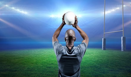 Rear view of african american male rugby player throwing a rugby ball against stadium in background. sports and fitness concept